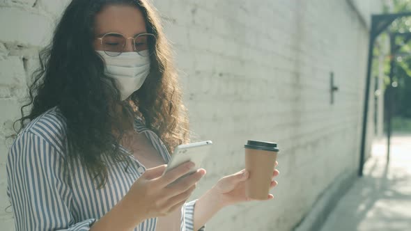 Slow Motion of Young Asian Lady Wearing Medical Face Mask Using Smartphone and Holding to Go Coffee