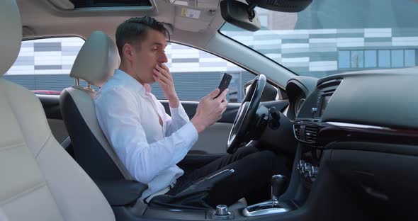 Shocked Businessman Scared By a Bad Message on His Smartphone Sitting in the Driver's Seat in the