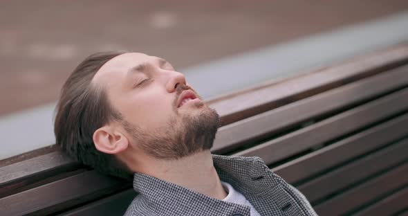 Young Man with Mustaches and a Beard Puts His Head on the Back of the Bench and Closes the Eyes in