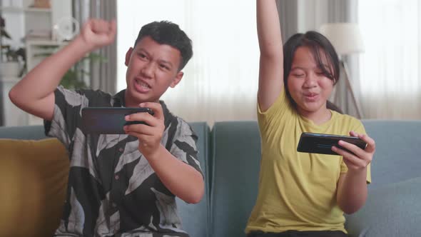 Asian Children Playing Video Games On Mobile Phone And Celebrating Victory At Home