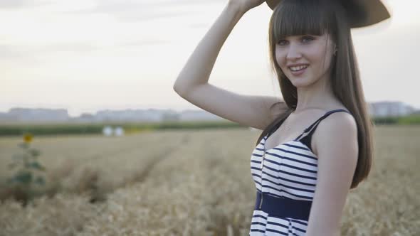 Happy Girl in Dress Whirling with Hat in Wheat Field