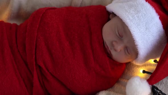 Top View Portrait First Days Of Life Newborn Cute Funny Sleeping Baby In Santa Hat Wrapped In Red