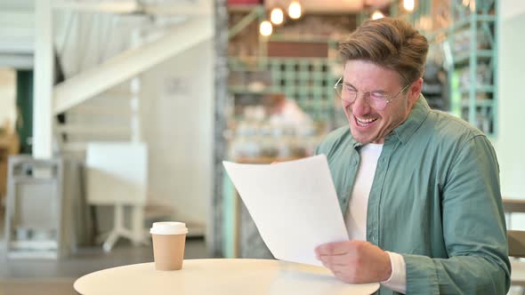 Middle Aged Man Celebrating Success on Documents in Cafe