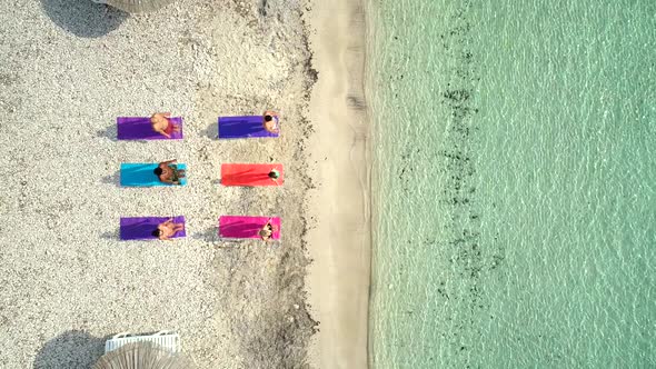 Aerial view of group of people doing yoga on colourful mats on the beach.