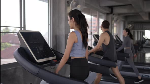 4K Group of Asian man and woman jogging on treadmill together at fitness gym.