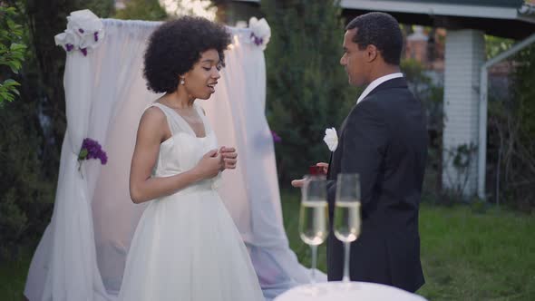 Medium Shot Side View of Young African American Man in Wedding Suit Opening Ring Box As Excited