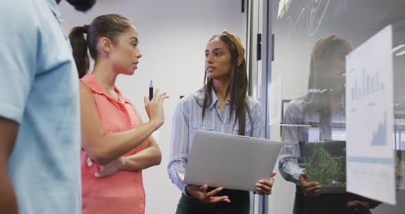 Diverse male and female business colleagues taking notes on glass wall and talking in office