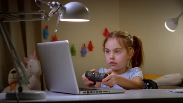 Cute Preschool Girl Playing Video Games with a Controller on a Laptop alt