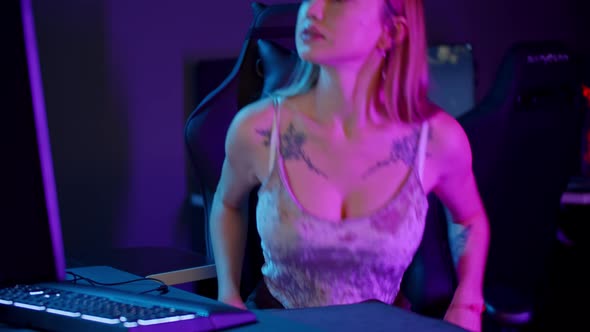 Tattooed Gamer Girl in Sexy Tank Top Sits By the PC - Putting on Her Headphones and Starts Playing