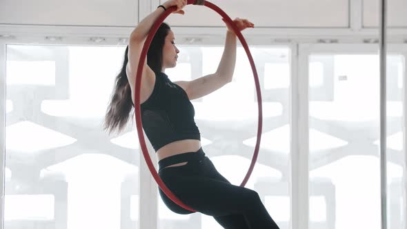 Gymnastic Training  Young Woman Sits on an Acrobatic Ring  Hanging Down with Her Head