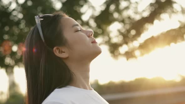 Asian woman relaxed enjoying peaceful sunset and looking up exhaling fresh air relaxing.