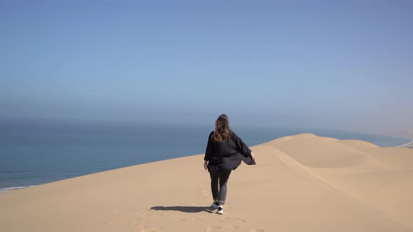 A Young Woman Walks Along Sandy Dunes on Seashore