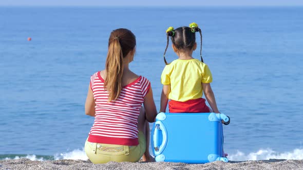 Little Cute Girl and Her Mom in Colorful Clothes Are Sitting on the Beach.