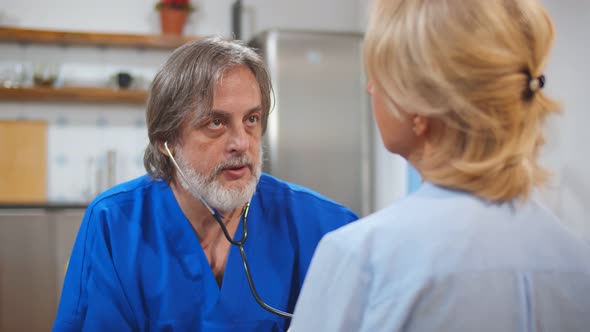 Mature Doctor Using Stethoscope To Examine Senior Female Patient Heart