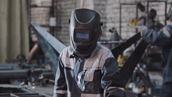 Young Man Working at the Plant Puts Down the Protective Helmet and About to Start Welding the Detail