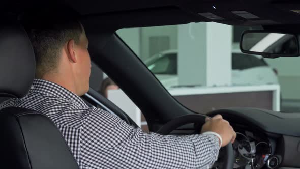 Handsome Man Smiling Over His Shoulder Showing Thumbs Up, Sitting in a New Car