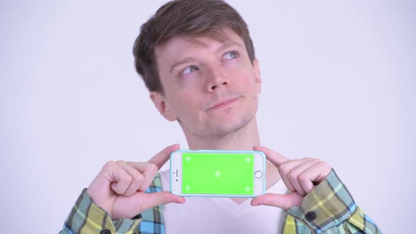 Face of Happy Young Handsome Man Thinking While Showing Phone
