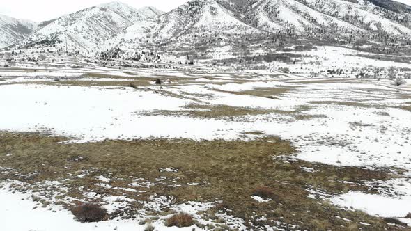 A reveal of a snow covered field at the base of a mountain in winter.