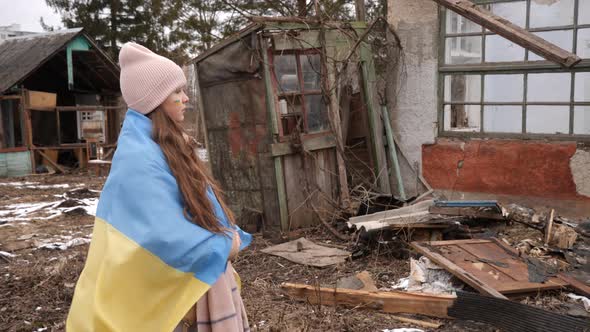 a girl wearing in the Ukrainian flag looks at the destroyed houses. War in Ukraine