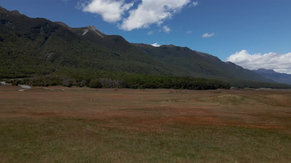 Aerial view of a car driving across an open grassy field in Fiordland Southland, New Zealand. Wide o