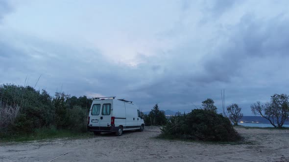 Time lapse of a camper van on the beach with rising moon and moving clouds during evening twilight,