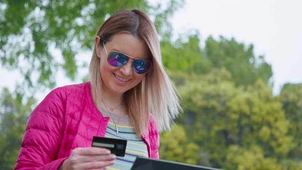 Happy Young Woman with Credit Card Using Instant Mobile Payments at Urban Park
