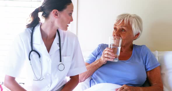 Female doctor serving a glass of water to senior woman in the bedroom