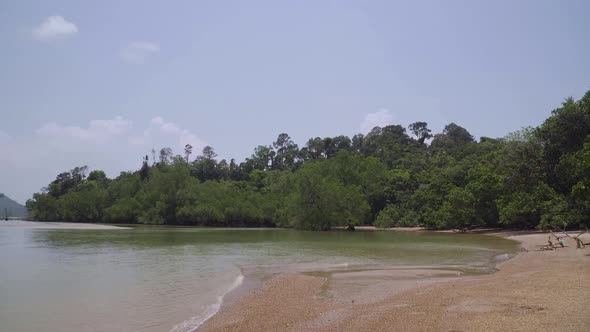 Tropical beach with sand, small island, tree, turquoise ocean against blue sky with clouds