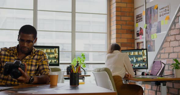 Male graphic designer reviewing photos on digital camera at desk 4k