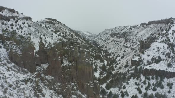 Tracking drone shot through snowy canyon with rocky bluffs