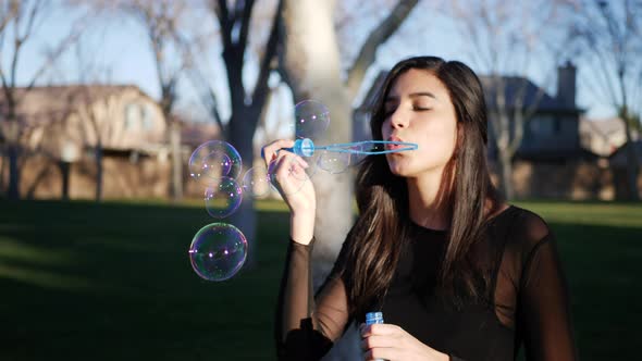 A beautiful girl blowing many dreamy bubbles in sunlight while smiling in a joyful way SLOW MOTION.