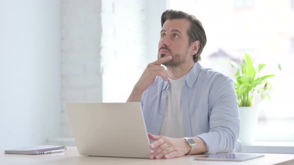 Young Man Thinking While Working on Laptop