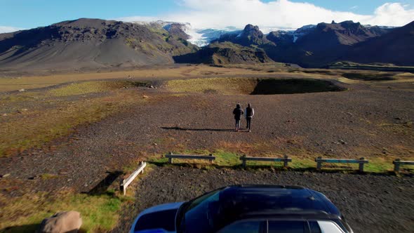 Aerial of a Car and Couple of Tourists on a Little View Point of Epic Mountains