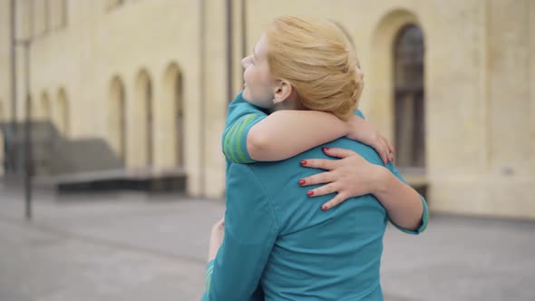 Back View of Young Blond Stewardess Hugging Blurred Brunette Colleague and Waving Goodbye. Slim