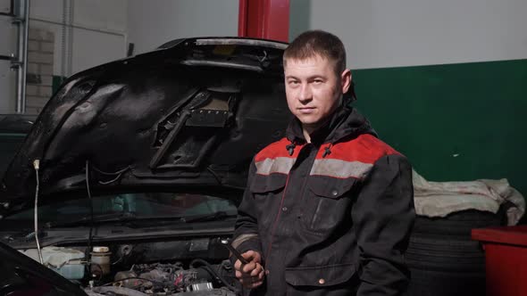 Technician with Wrench in Hand Stands and Smilesnear Renovated Automobile with Open Bonnet