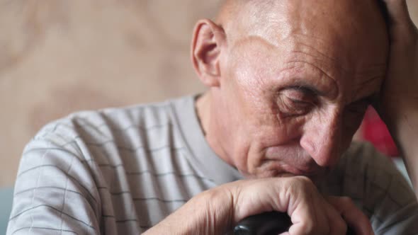 Caucasian elderly man sad 70-79 years old with a walking stick sits and meditates holding his head w