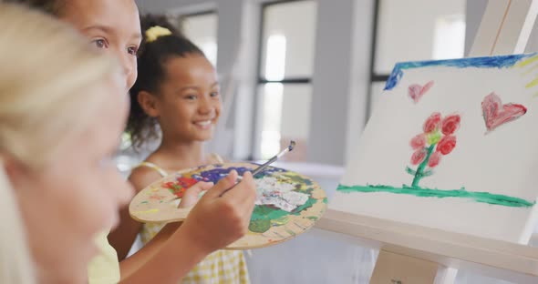 Video of happy diverse girls painting during art lessons at school