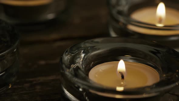 Tea candles with flaming wicks on a wooden background - CANDLES 009