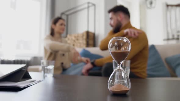 Sand Clock Counting Time while Young Raging Married Couple Quarreling