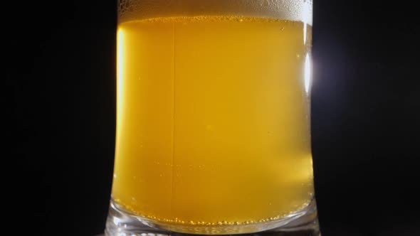 Closeup of a Glass of Light Beer Slowly Rotating on a Black Background