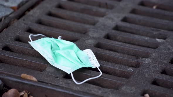 A simple green protective Covid-19 face mask lying thrown out on a rusty sewerage hatch amongst dry