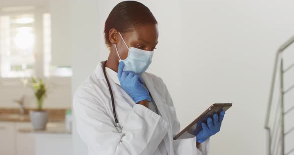 African american female doctor wearing mask having video call consultation using digital tablet