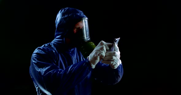 Portrait of a Man in a Blue Protective Suit, White Gloves and a Gas Mask on a Black Background. He