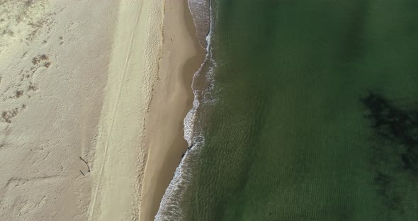 Aerial view of tropical beach, foamy ocean waves washing sand. Waves hitting sand beach