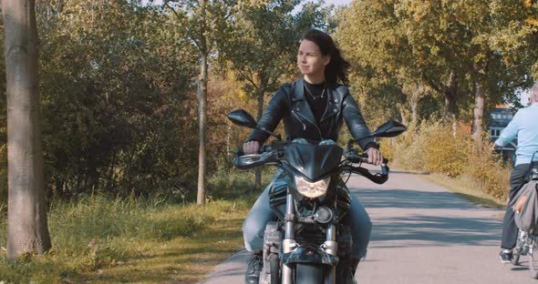 Front view of beautiful smiling European Female motorcyclist wearing leather driving On road passing