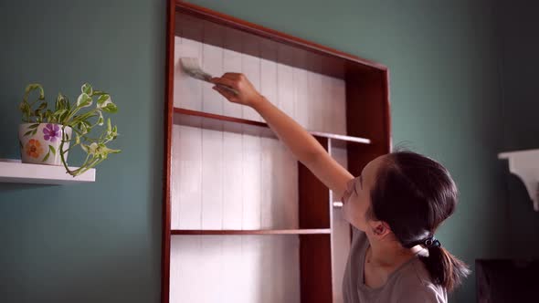 Asian woman painting wooden shelves at home