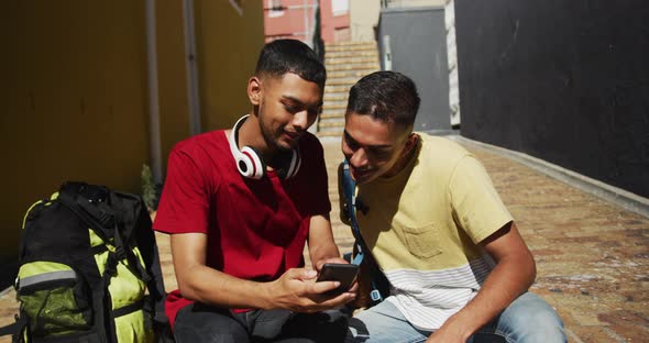 Two mixed race friends sitting and using smartphone in the street
