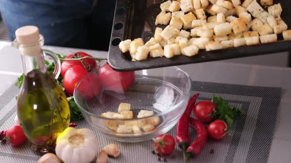 Making Caesar Salad  Pouring Bread Croutons From Baking Tray to Glass Bowl