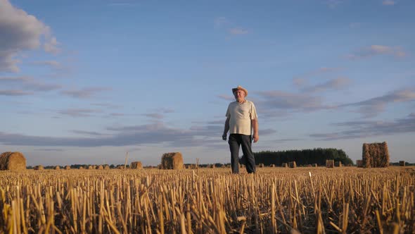 Farmer Agronomist Walking Through Agricultural Field With Haystacks At Sunset