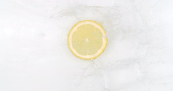 On a White Background, a Splash of Water Falls on a Slice of Lemon in Slow Motion